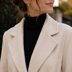 Dettaglio del revers ampio del cappotto beige indossato su un dolcevita nero
