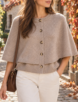 Cardigan beige in maglia con mantellina sovrapposta e bottoni, indossato con pantaloni bianchi