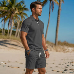 Polo grigio scuro manica corta e shorts coordinati tra le palme in spiaggia