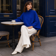Donna seduta al caffè con maglione blu dolcevita dalle ampie maniche svasate