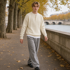 Uomo cammina indossando maglione bianco intrecciato con pantaloni grigi ampi