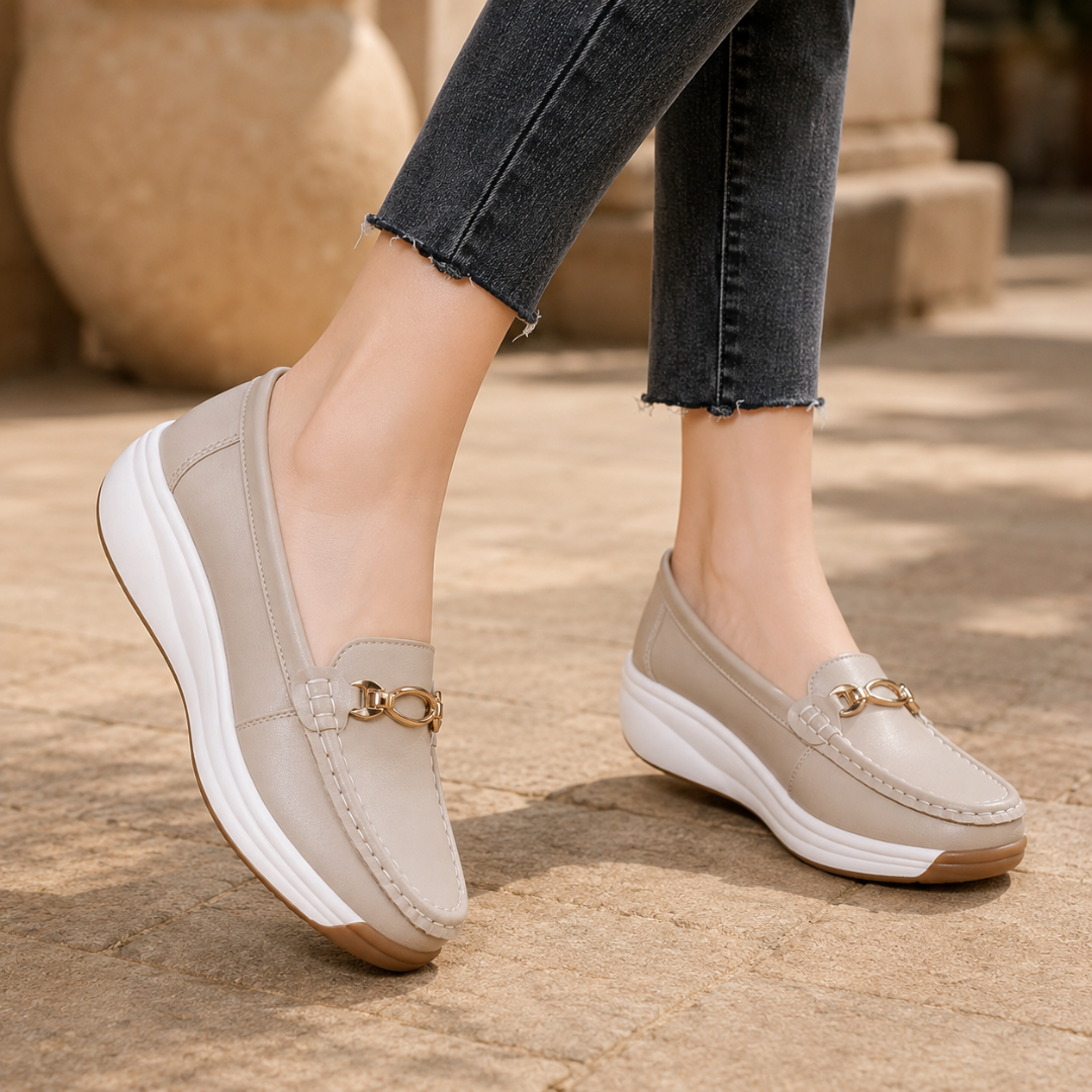 Mocassini beige indossati con pantaloni scuri, morsetto dorato in evidenza