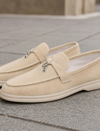Mocassini beige slip on con pendente metallico e suola chiara su pavimentazione urbana