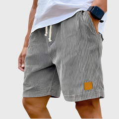 Pantaloncini uomo grigi a coste indossati con t-shirt bianca e mano in tasca