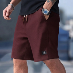 Pantaloncini uomo bordeaux indossati, taglio rilassato e piccola etichetta scura