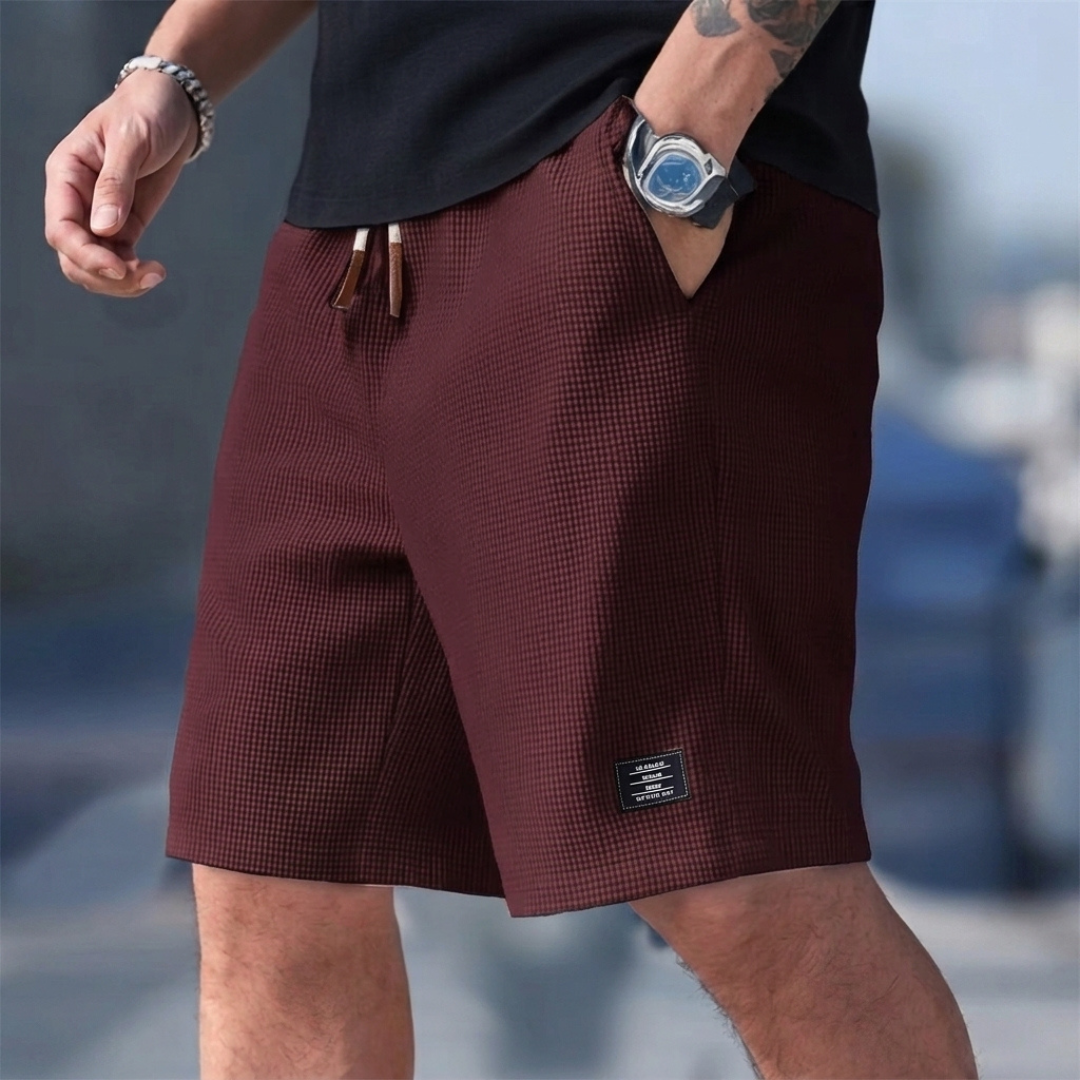 Pantaloncini uomo bordeaux indossati, taglio rilassato e piccola etichetta scura
