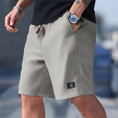 Pantaloncini uomo grigi indossati con mano in tasca e piccola etichetta laterale