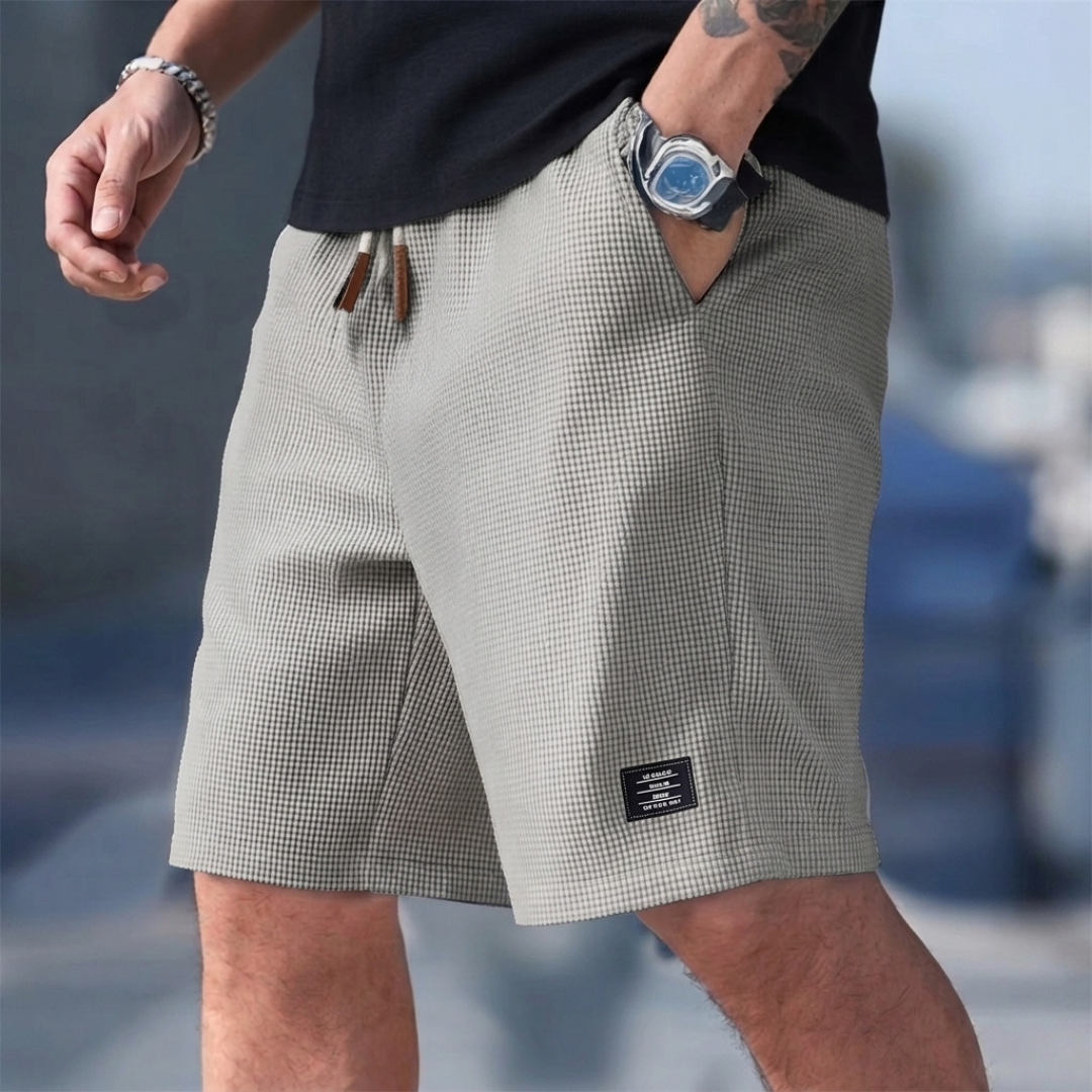 Pantaloncini uomo grigi indossati con mano in tasca e piccola etichetta laterale