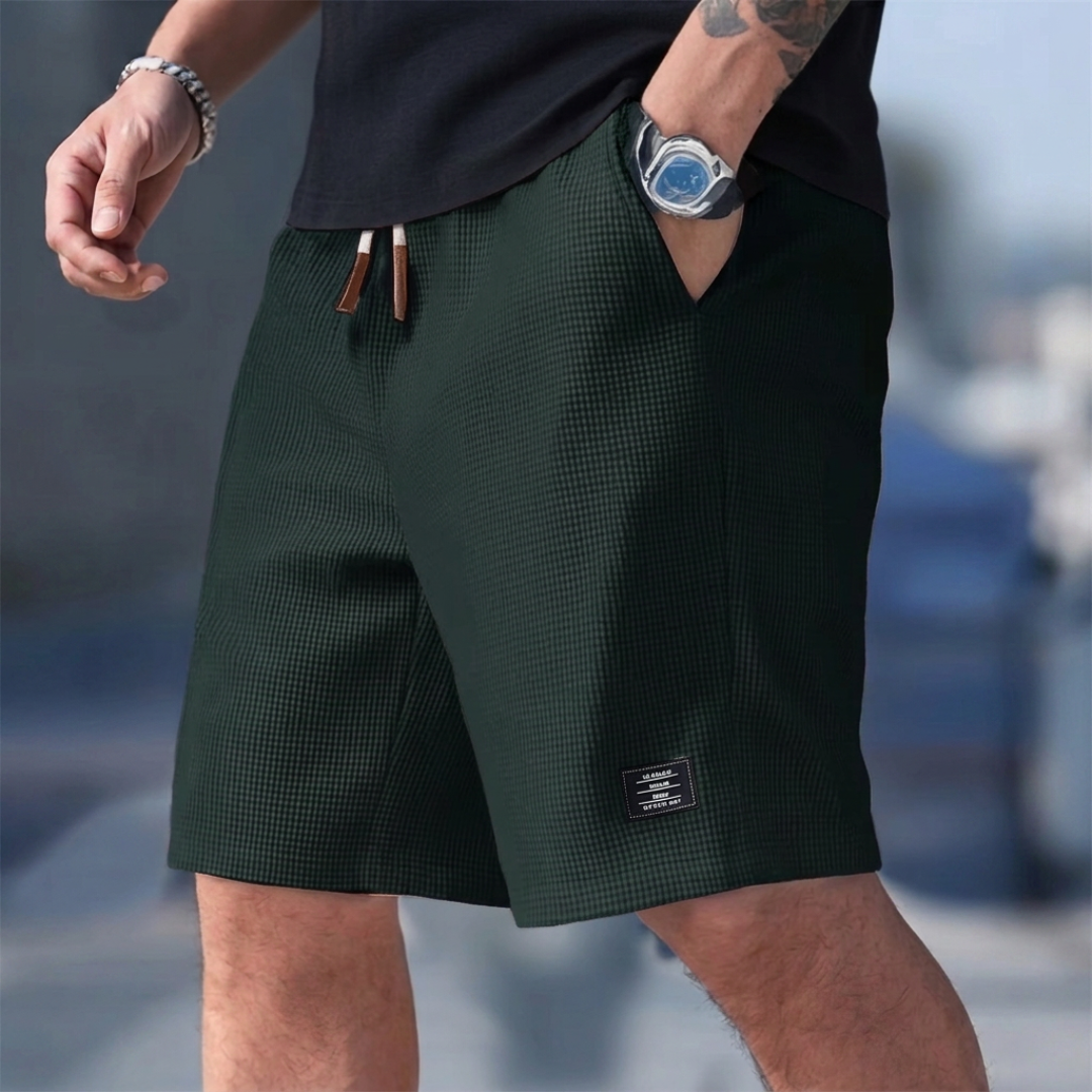 Pantaloncini uomo verde scuro indossati, lunghezza al ginocchio ed etichetta laterale