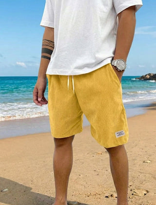 Pantaloncini uomo gialli a coste con coulisse bianca in vita, indossati in spiaggia