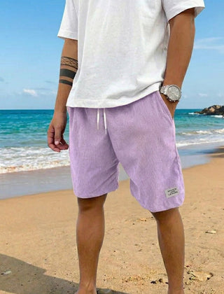 Pantaloncini uomo lilla a coste abbinati a t-shirt bianca oversize sulla sabbia