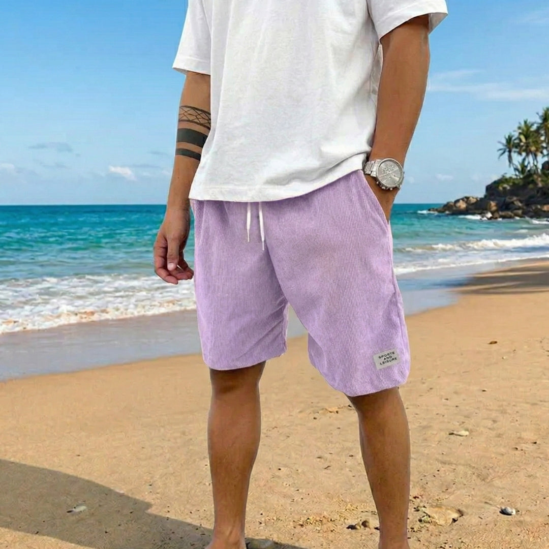 Pantaloncini uomo lilla a coste abbinati a t-shirt bianca oversize sulla sabbia
