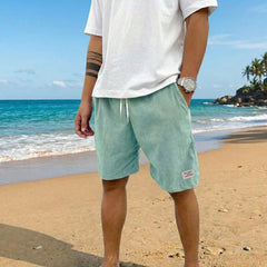 Pantaloncini uomo verde chiaro a coste con coulisse, indossati scalzi sulla spiaggia