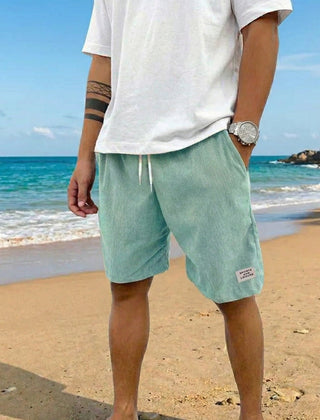 Pantaloncini uomo verde chiaro a coste con coulisse, indossati scalzi sulla spiaggia