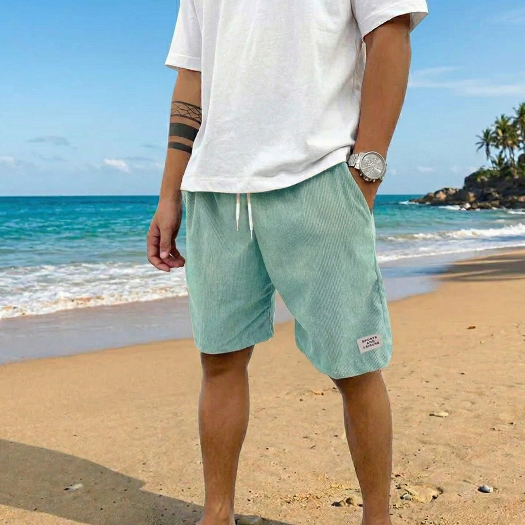 Pantaloncini uomo verde chiaro a coste con coulisse, indossati scalzi sulla spiaggia