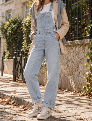 Salopette donna azzurra con pettorina e tasca frontale, orli arrotolati e sneakers chiare