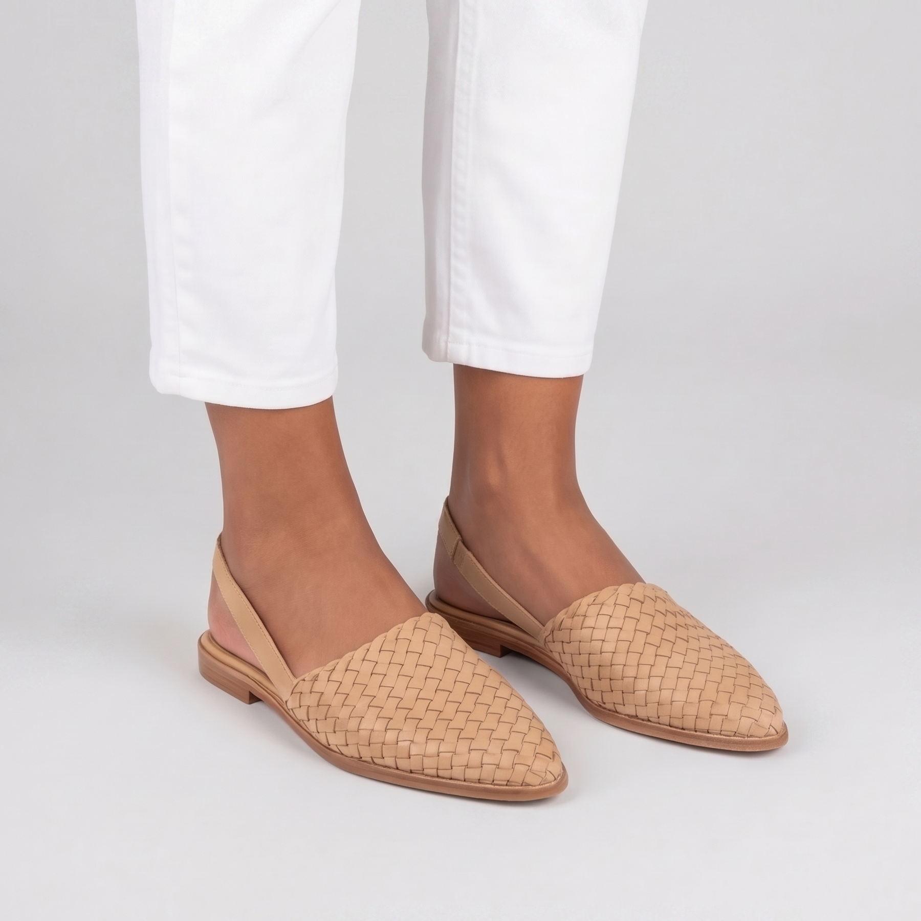 Slingback beige intrecciate con cinturino posteriore, indossate con pantaloni bianchi