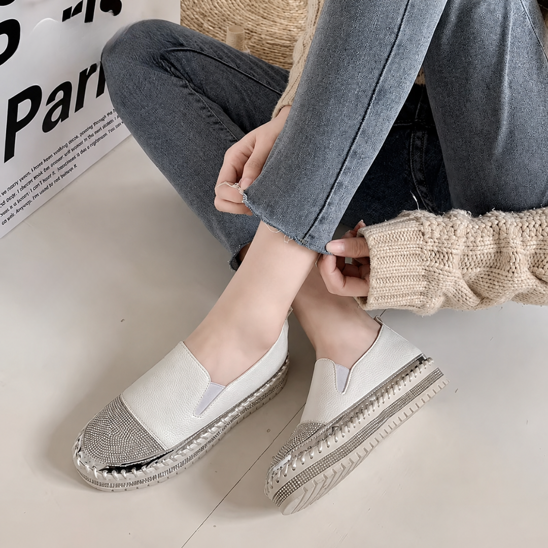Slip-on bianche indossate con pantaloni alla caviglia, suola platform con strass e cuciture