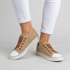 Sneakers donna beige slip-on indossate con pantaloni bianchi, punta bianca e banda a righe