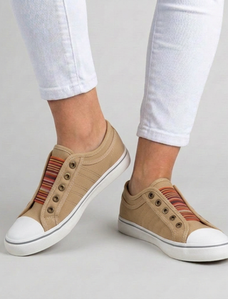 Sneakers donna beige slip-on indossate con pantaloni bianchi, punta bianca e banda a righe