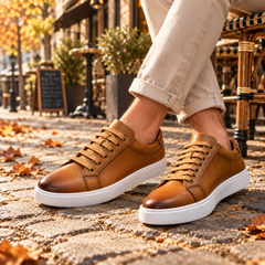 Sneakers basse caramello con occhielli metallici e lacci piatti su pavimentazione autunnale