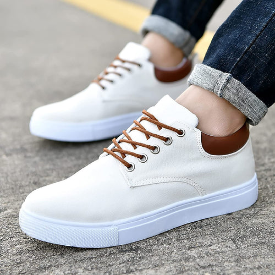 Sneakers bianche da uomo indossate con pantaloni scuri, lacci marroni ben visibili