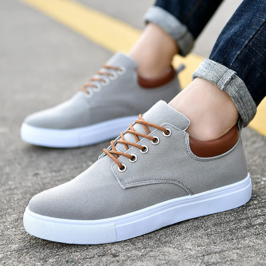 Sneakers grigie da uomo indossate con pantaloni risvoltati, occhielli metallici in evidenza
