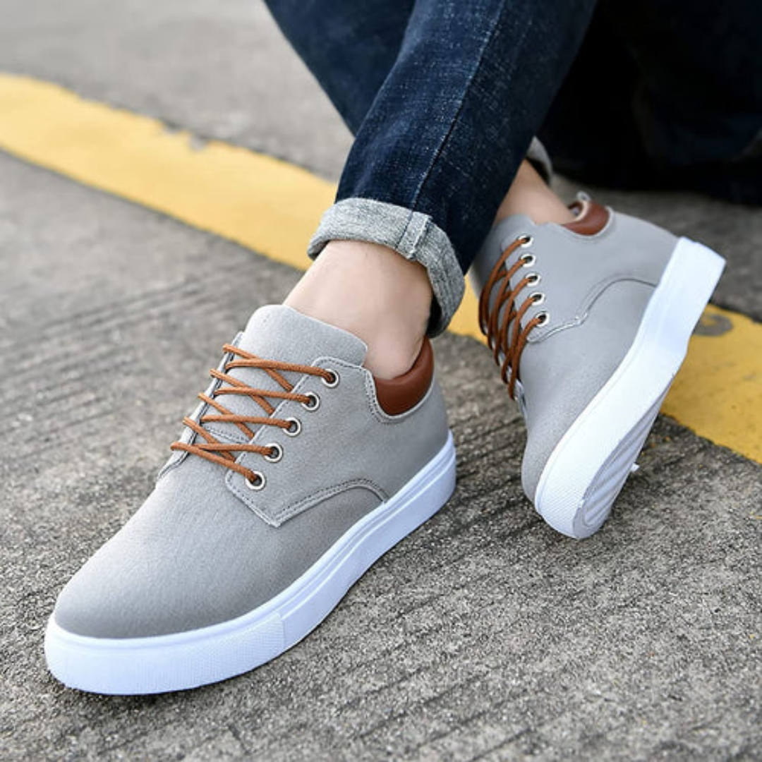 Sneakers grigie uomo con talloncino marrone e suola bassa, piede appoggiato al cordolo