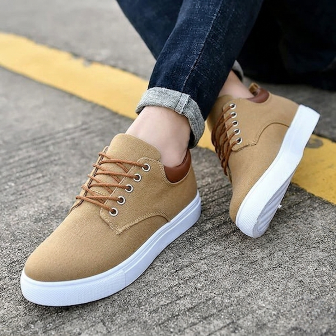 Sneakers marroni uomo con suola bassa bianca, piede appoggiato sul cordolo giallo