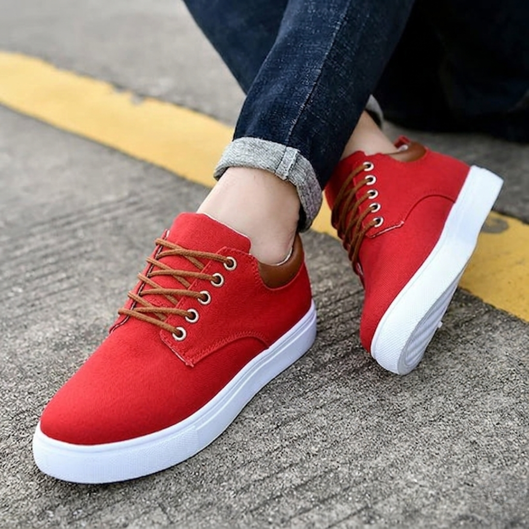Sneakers rosse uomo con suola bianca spessa, piede sollevato sul bordo marciapiede