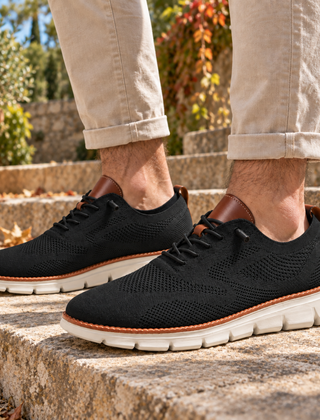 Sneakers uomo nere in maglia traforata con suola bianca su gradini in pietra