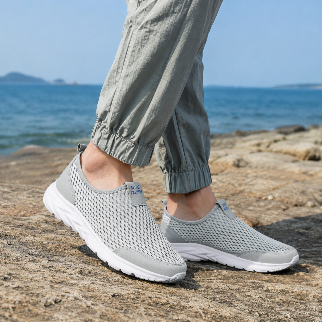 Uomo indossa sneakers slip-on grigie traforate con pantaloni chiari in riva al mare