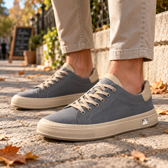 Sneakers uomo grigie con lacci chiari e suola a contrasto, indossate su pavimentazione in pietra
