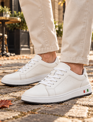 Sneakers uomo bianche con lacci e suola bicolore indossate su pavimentazione in pietra