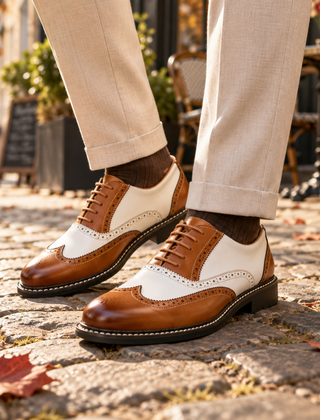 Scarpe stringate uomo marroni e bianche con forature brogue, indossate con pantaloni beige