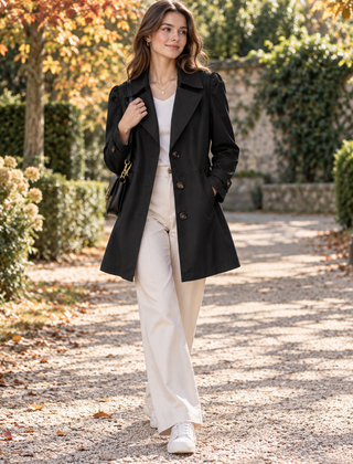 Trench donna nero con bottoni a vista e cinturini ai polsini, in giardino