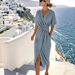 Vestito midi azzurro con nodo drappeggiato in vita e spacco frontale, indossato in terrazza sul mare